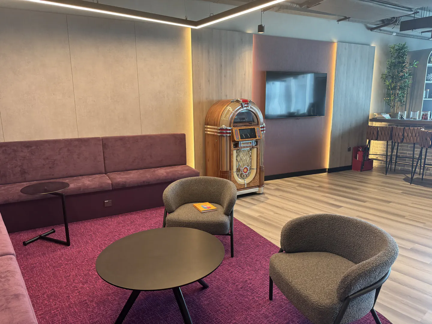 Interior view of a lounge area with a purple sofa, two gray chairs, a black table, and a vintage jukebox.
