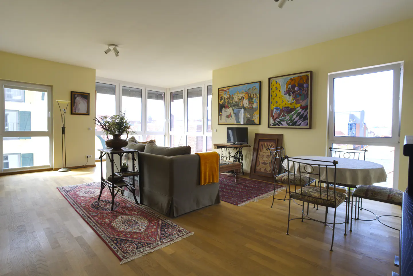 A living room with hardwood floors, a gray sofa, a round table with four chairs, and two paintings on the wall.