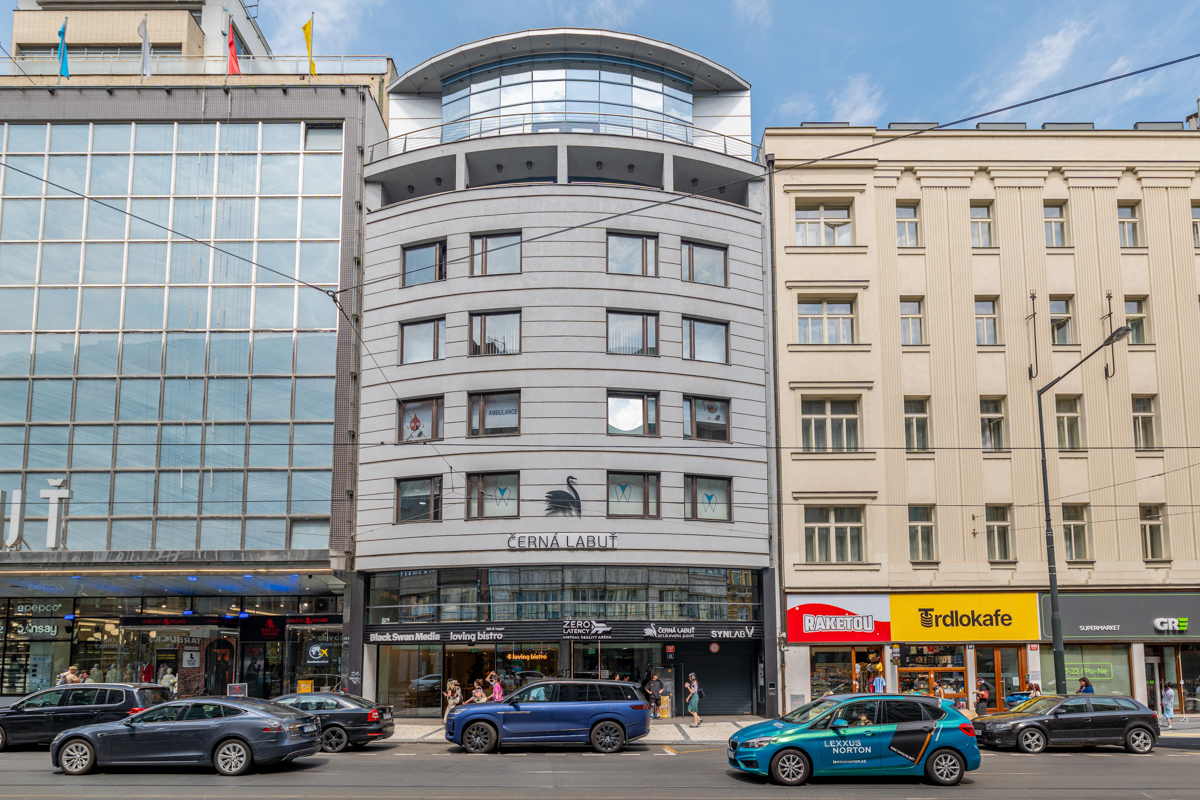 A modern grey building with a black swan logo sits between a glass-fronted office building and a classic cream building. [AI-generated text]