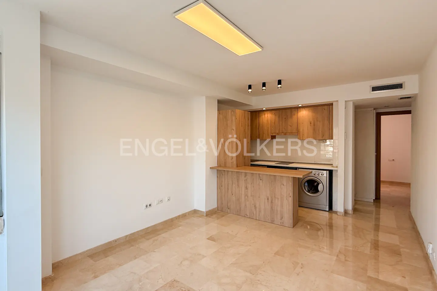 A bright apartment interior with marble floors, a wood kitchen, and an Engel & Völkers logo on the wall.