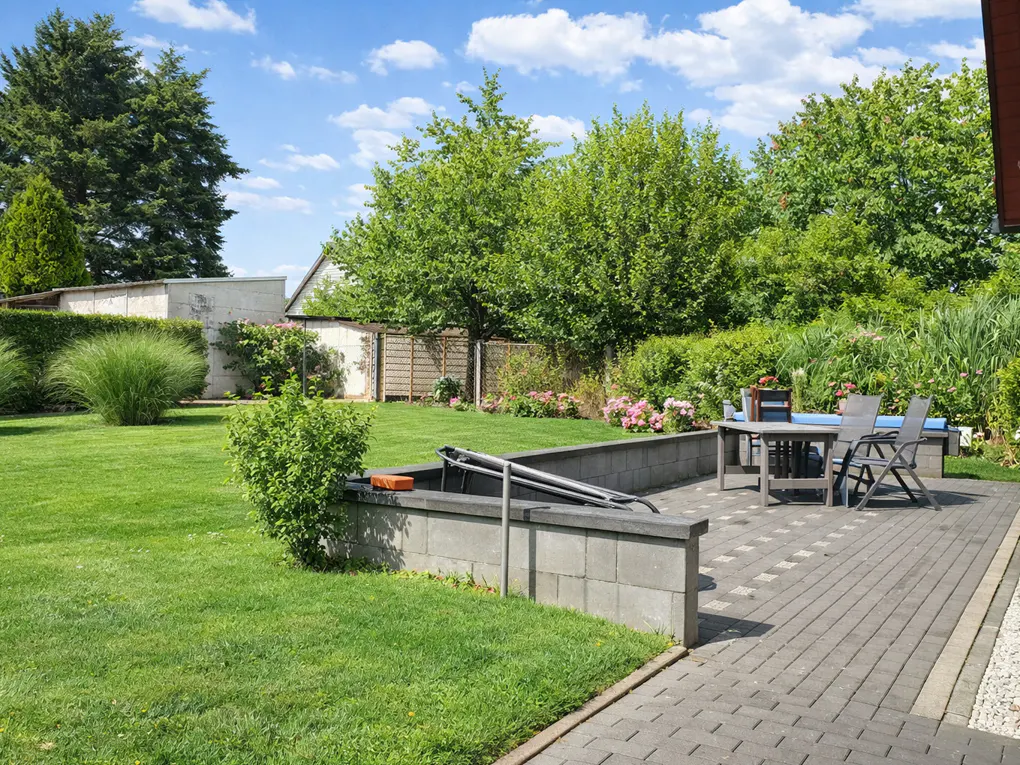 A backyard with green grass, trees, and a patio with a table and chairs.