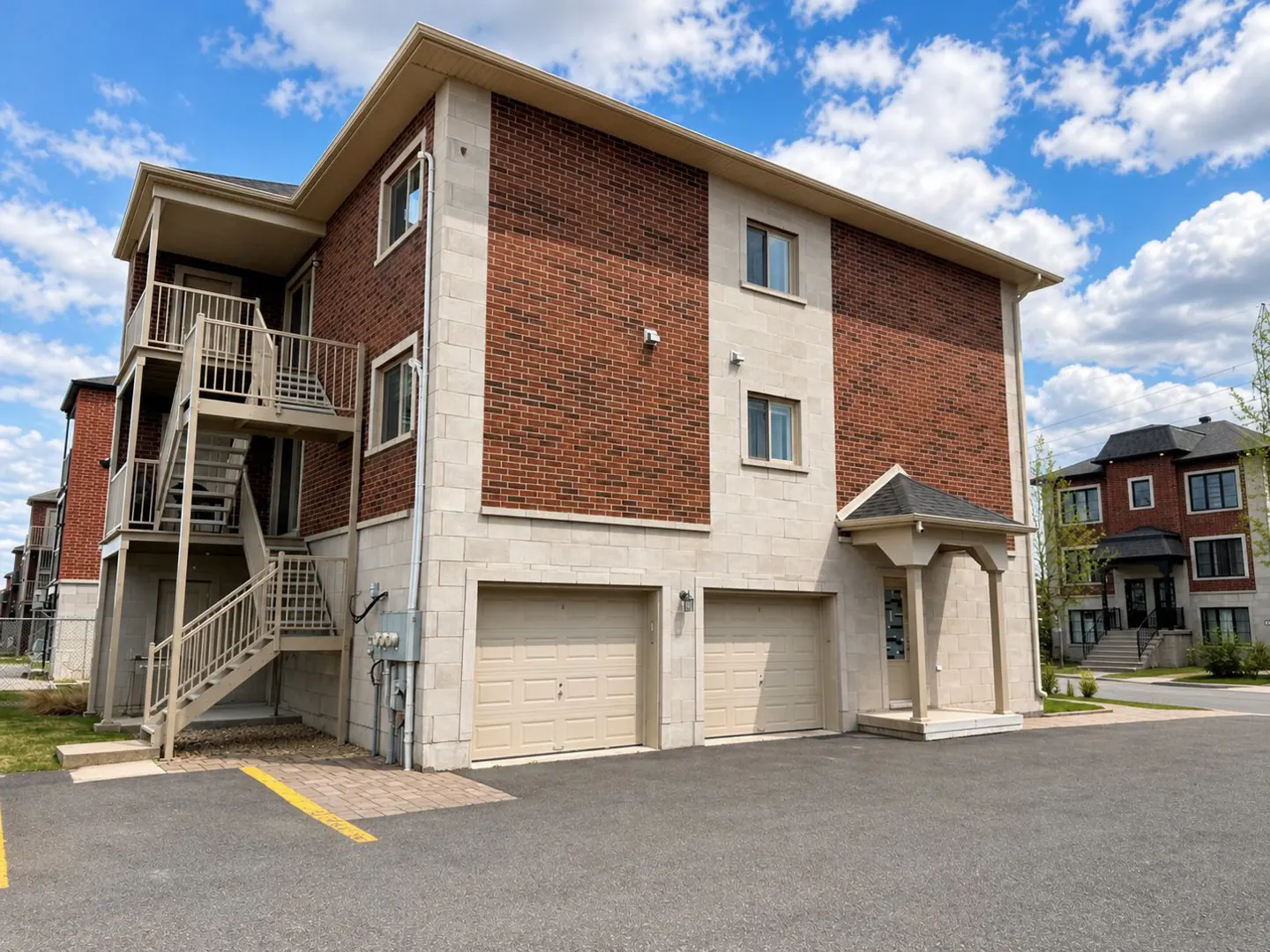 Exterior view of a three-story apartment building with brick and stone facade, two garage doors, and an outdoor staircase.