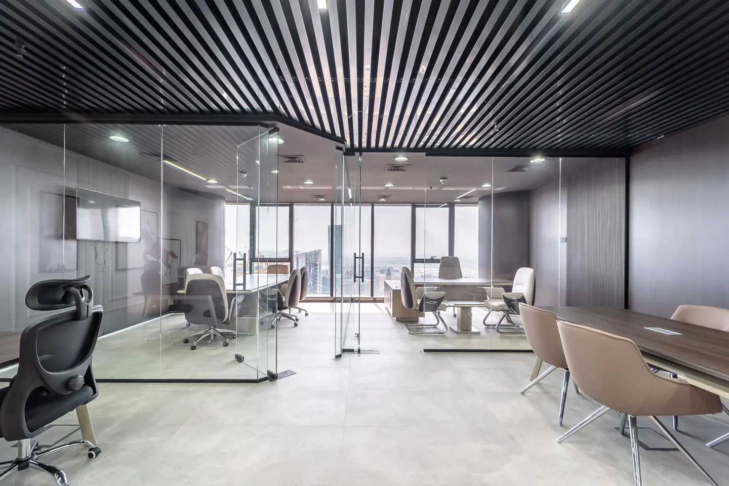 Modern office space with glass walls, a black slatted ceiling, and neutral-toned furniture. City view visible through large windows.