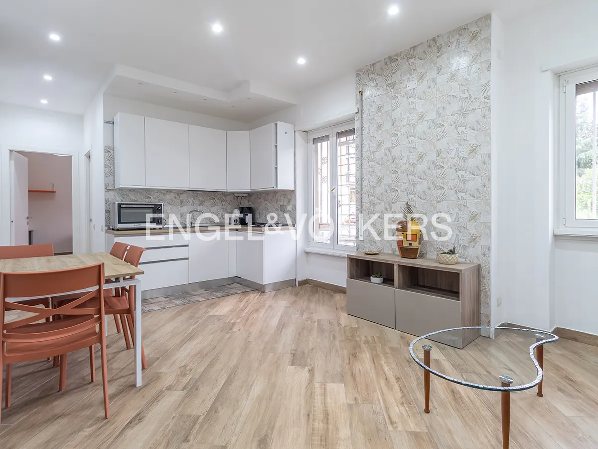 Bright, modern kitchen with white cabinets, wood floors, and a dining table with orange chairs. A glass coffee table sits in the living area.