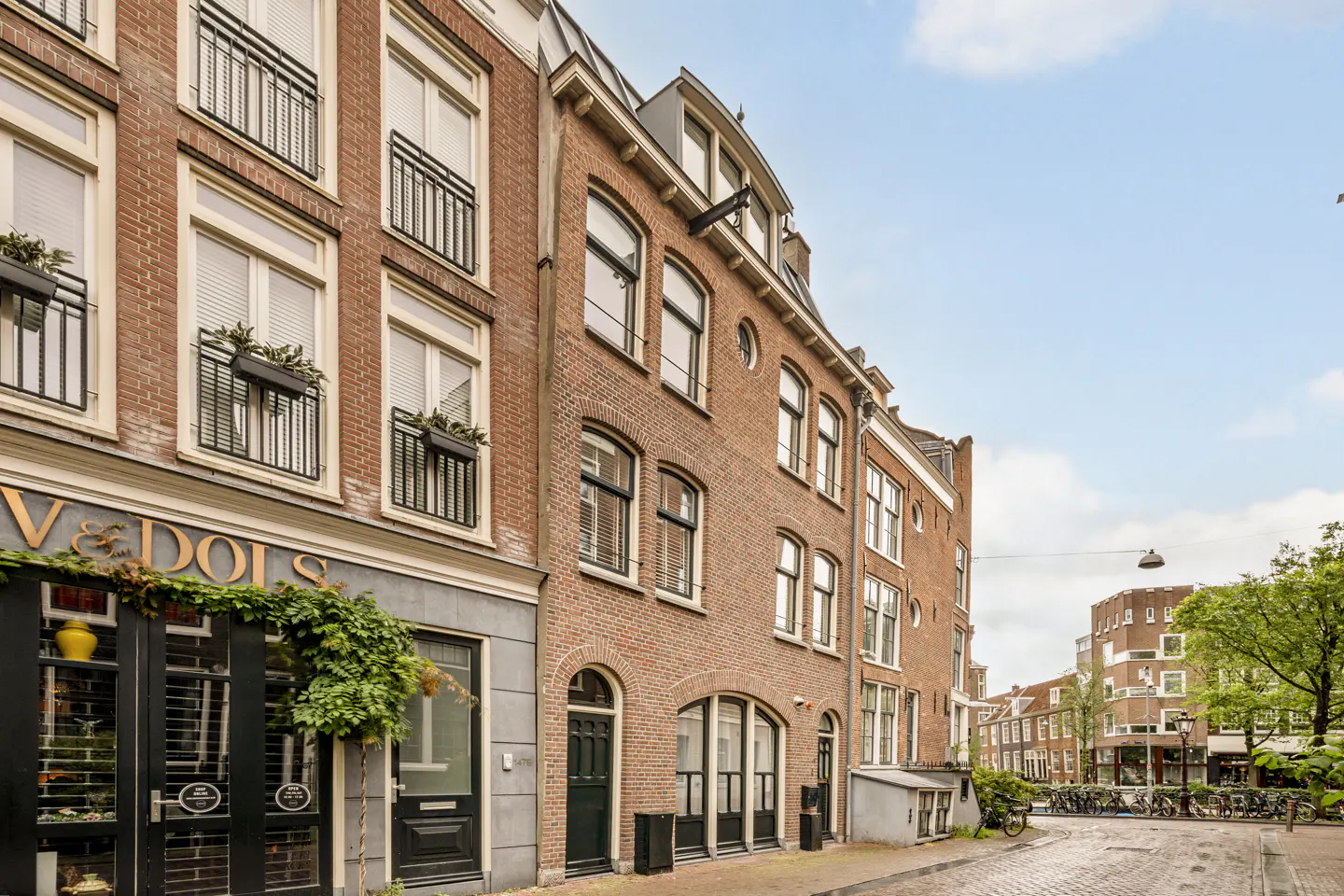 A row of historic brick buildings in a European city with black-framed windows, balconies, and a storefront on the left.