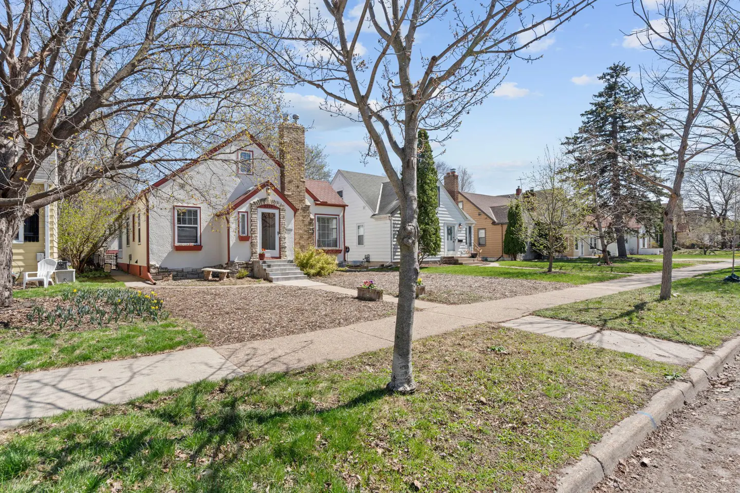 A street view of houses with green lawns and trees under a blue sky.
