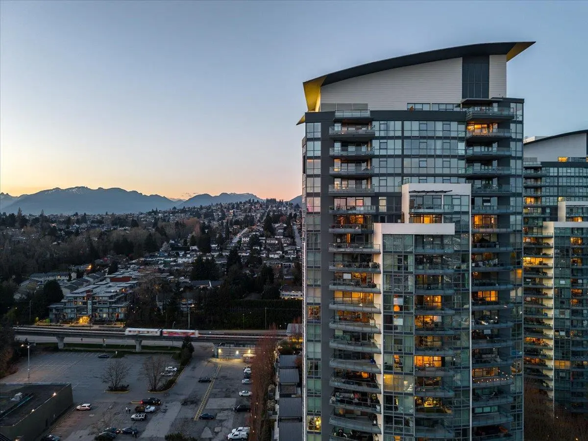 View of modern high-rise condos with balconies, a train, and mountains at dusk.