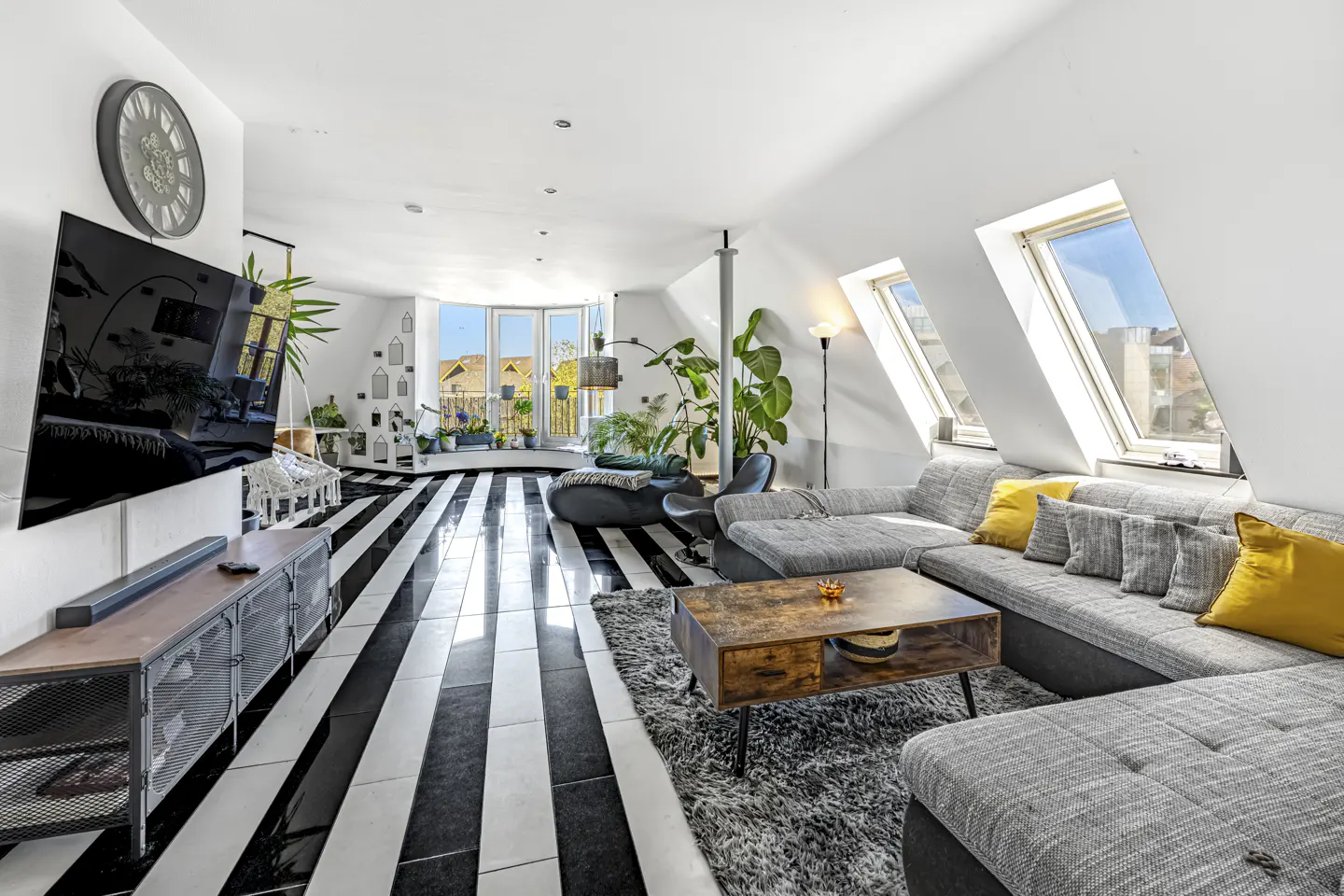Bright living room with black and white striped floors, gray sofa with yellow pillows, and large windows.