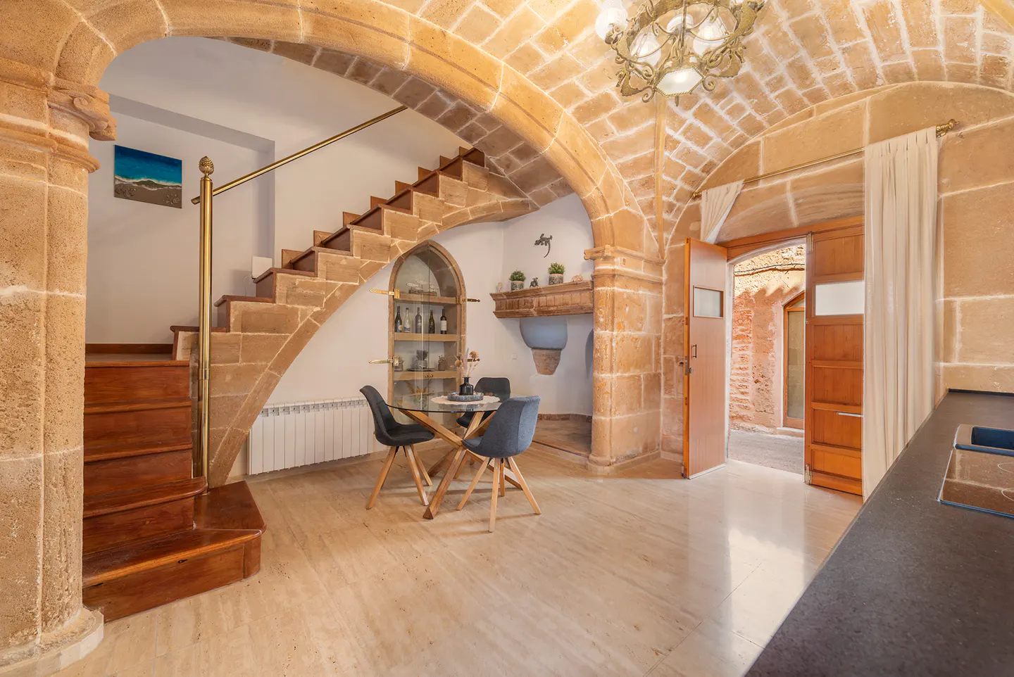 Interior view of a stone-walled room with stairs, a dining table, and an open doorway to an outdoor area.