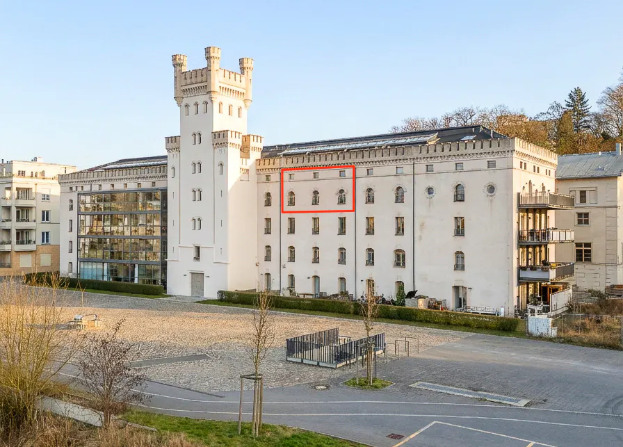 Exterior view of a large, white building with a tower, multiple windows, and a courtyard.
