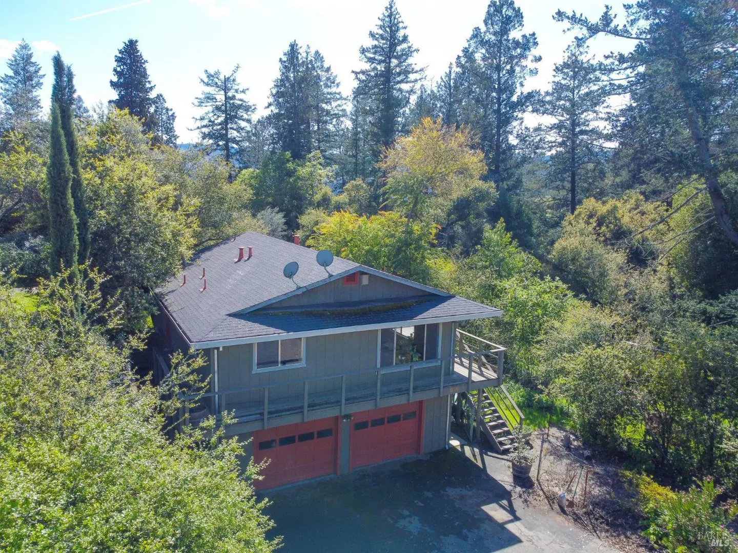Two-story house with gray siding, red garage doors, and a deck, surrounded by trees.