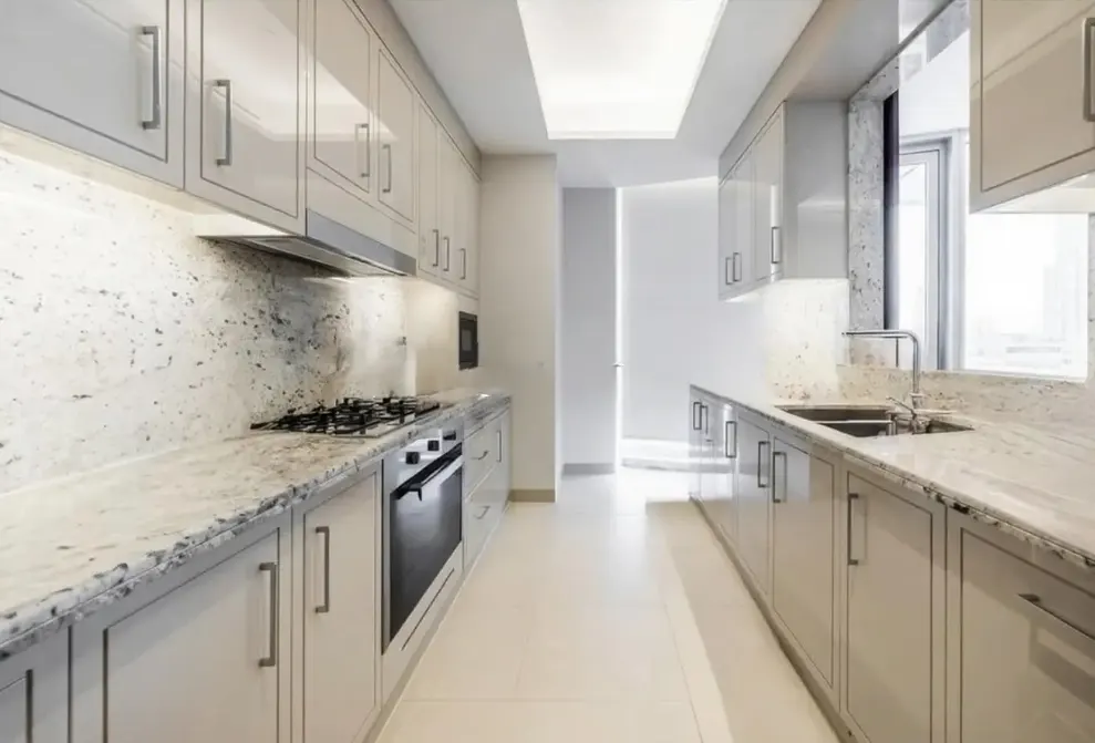 Modern galley kitchen with glossy light gray cabinets, speckled granite countertops, and stainless steel appliances.