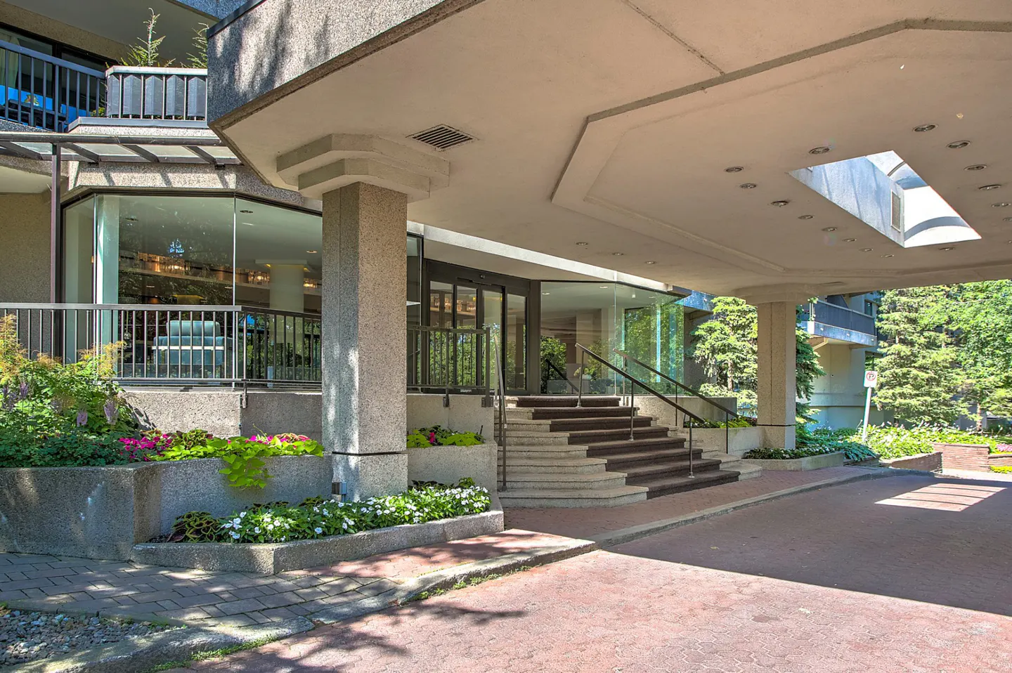 Exterior view of a condo building entrance with concrete columns, steps, glass doors, and flower beds.