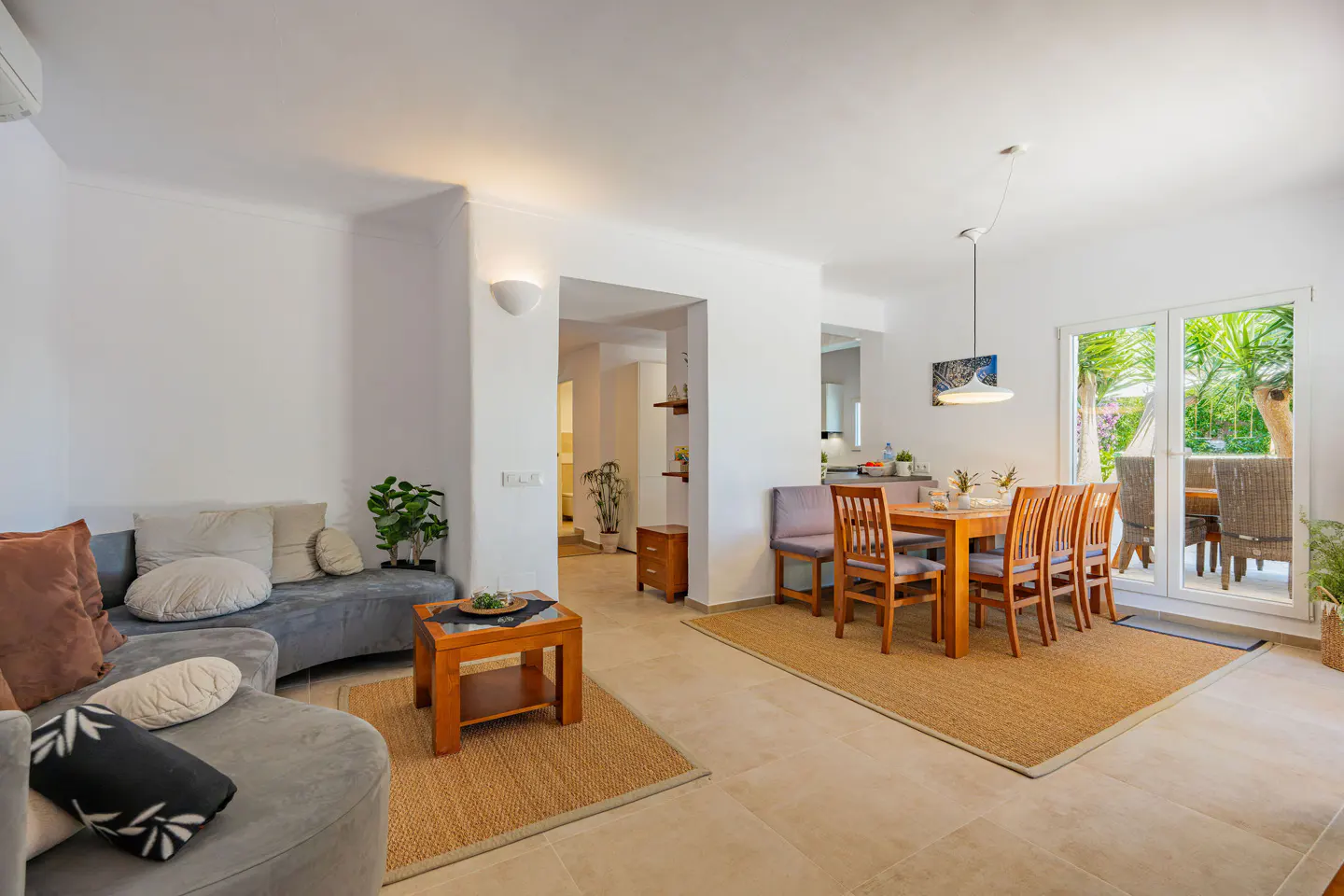 Bright open-plan living and dining area with grey sofa, wooden coffee table, and dining set leading to a patio.