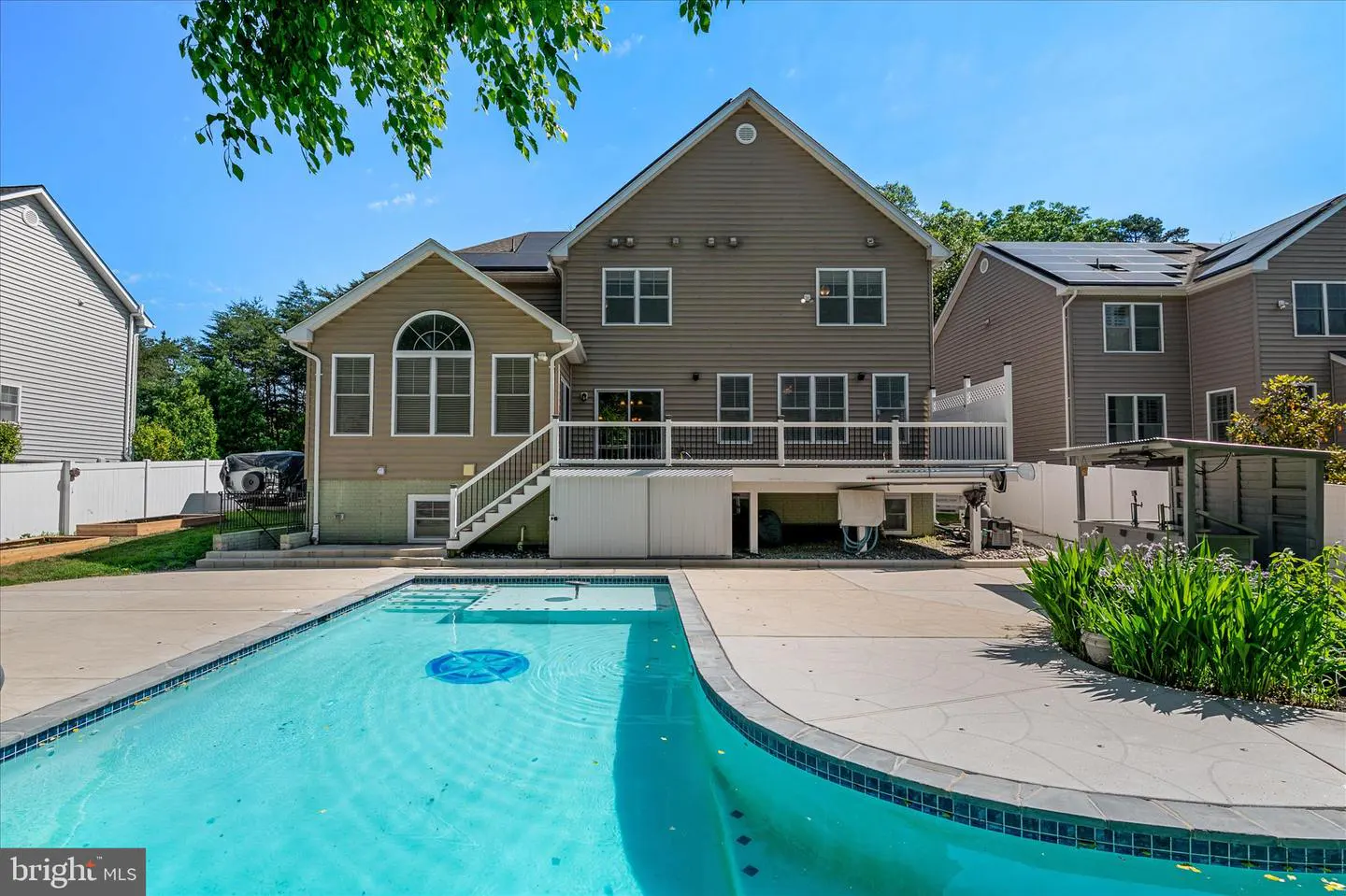 Backyard view of a two-story house with a blue swimming pool and a white deck. The house is light brown with white trim.