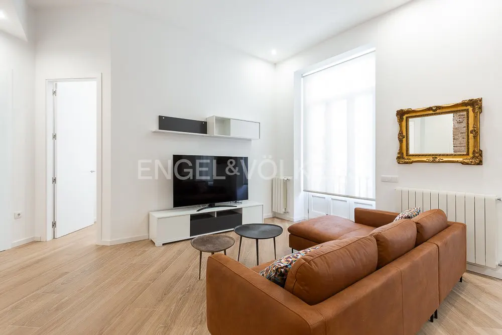 Bright living room with a brown leather sectional sofa, TV, and gold-framed mirror on a white wall.