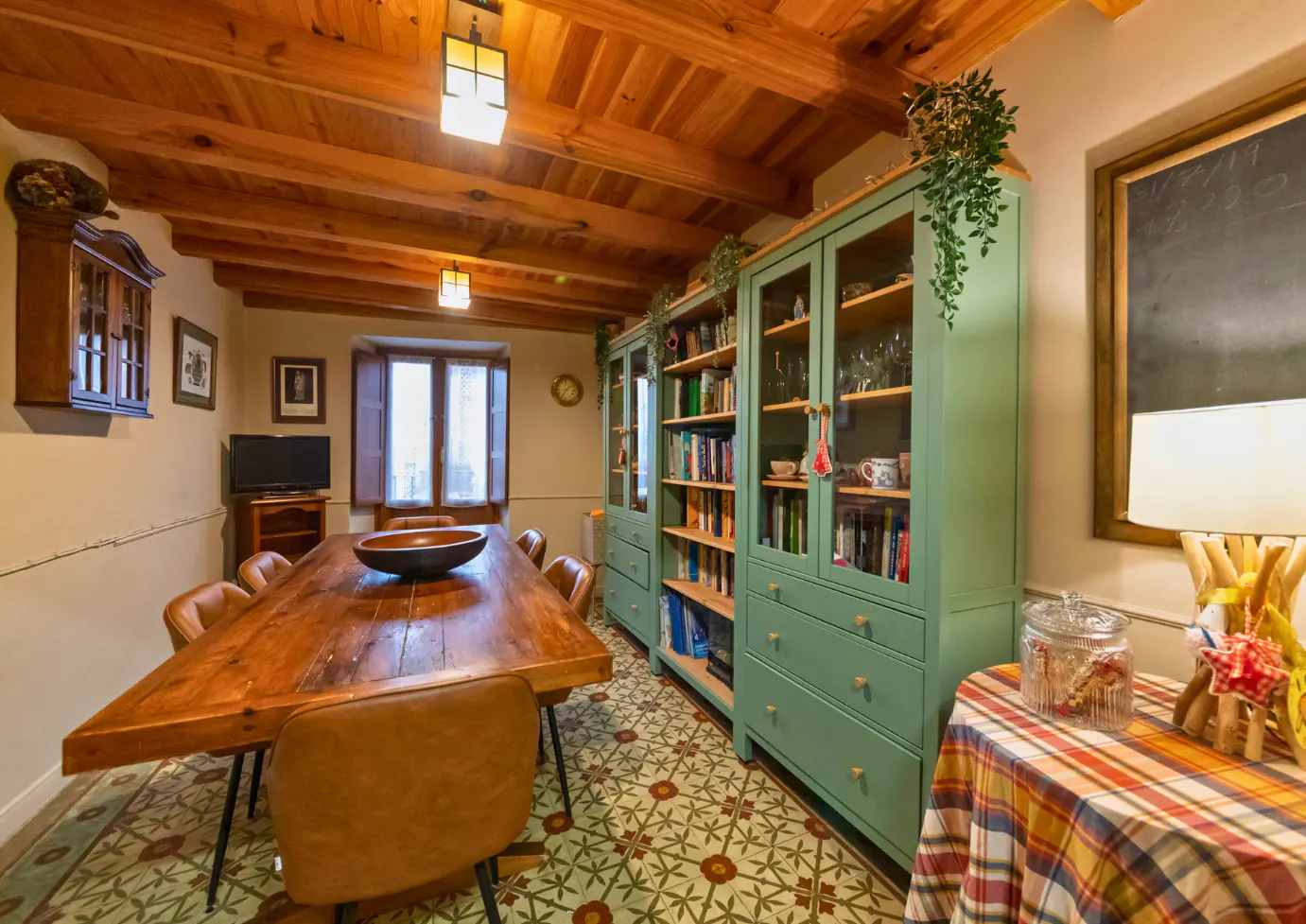 A dining room with a wooden table, leather chairs, green cabinets, and a patterned floor.