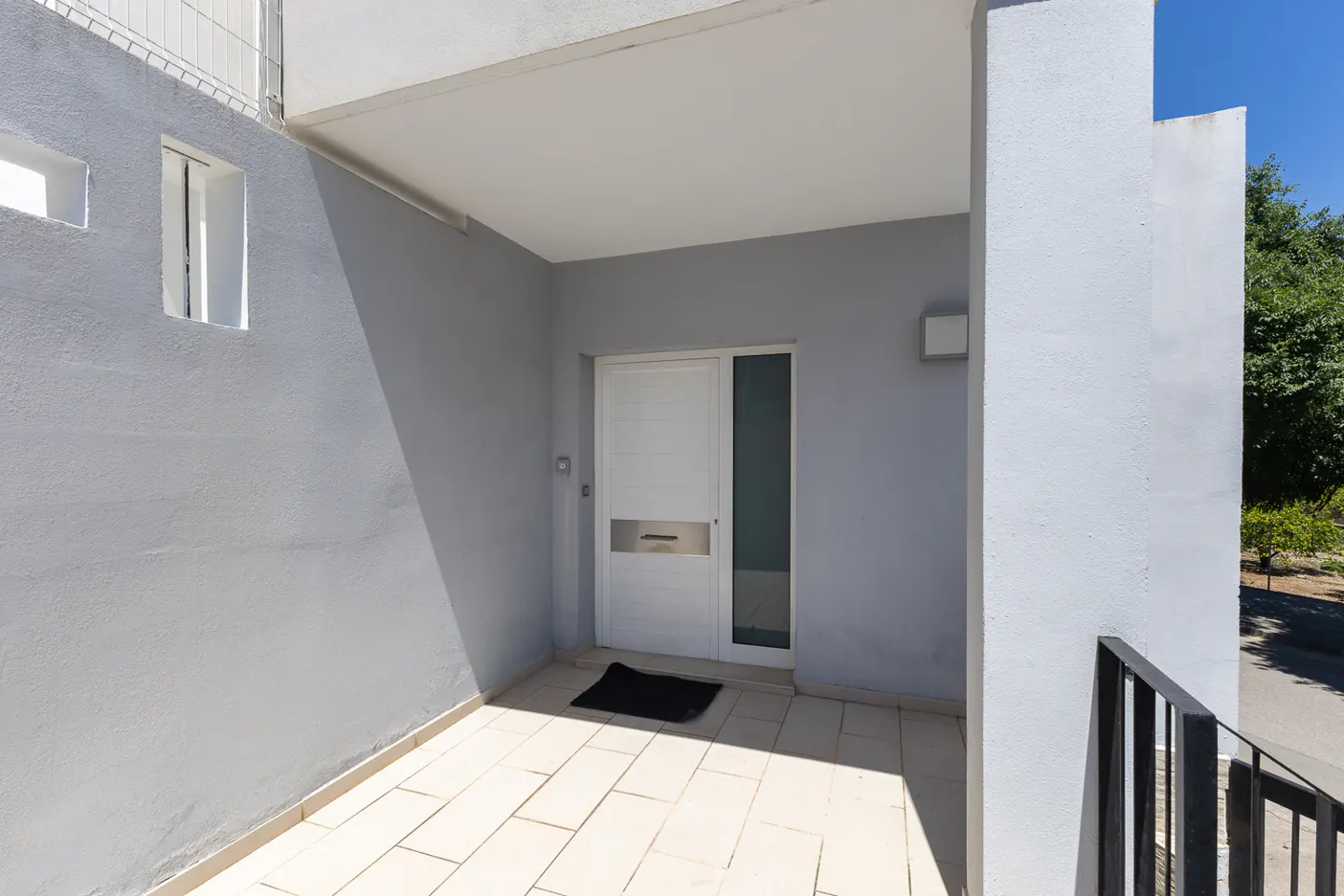 Exterior view of a gray building with a white door, small windows, and a tiled porch.
