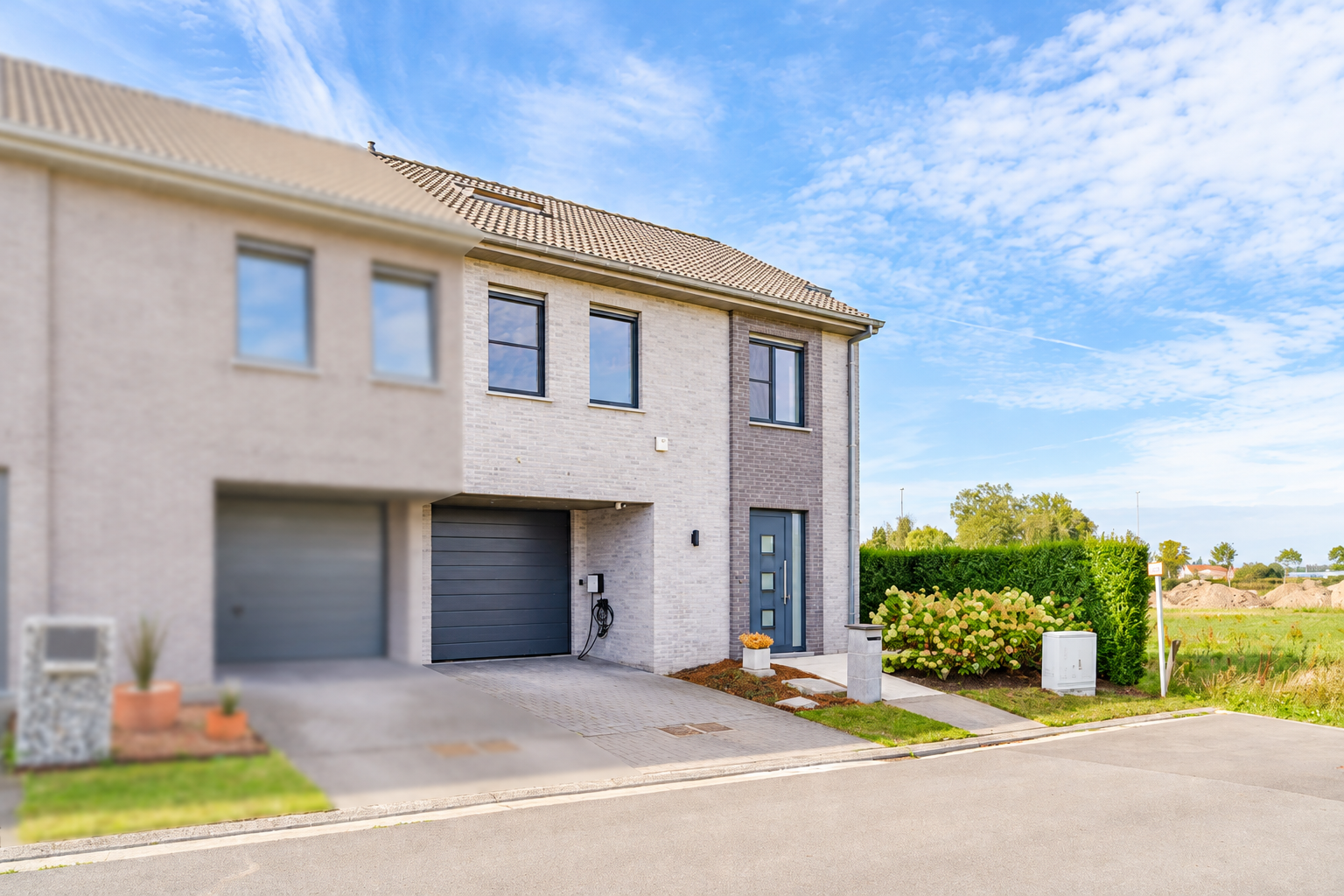 Modern two-story townhouse with light brick facade, dark grey garage door, and blue front door under a bright blue sky. [AI-generated text]