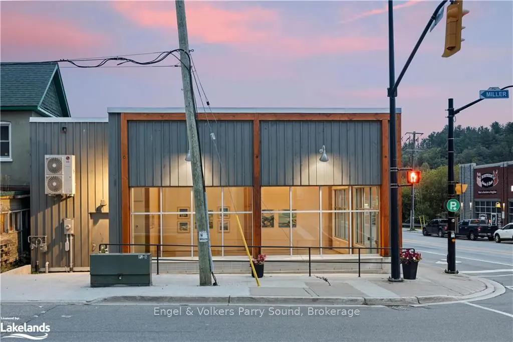 Exterior view of a gray building with large windows, wood trim, and a black railing, on a street corner with traffic lights.