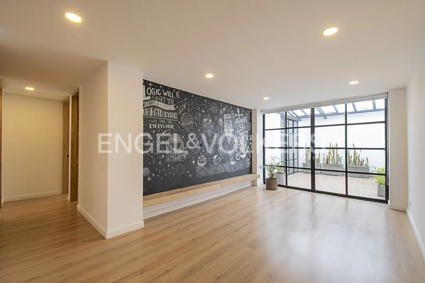 Bright, modern room with wood floors, a chalkboard wall with white drawings, and a black-framed window to an outdoor patio.