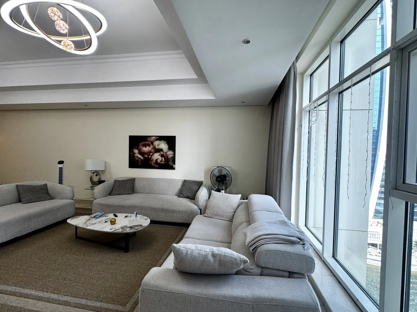 A modern living room with light gray sofas, a marble coffee table, and a large window with city views.