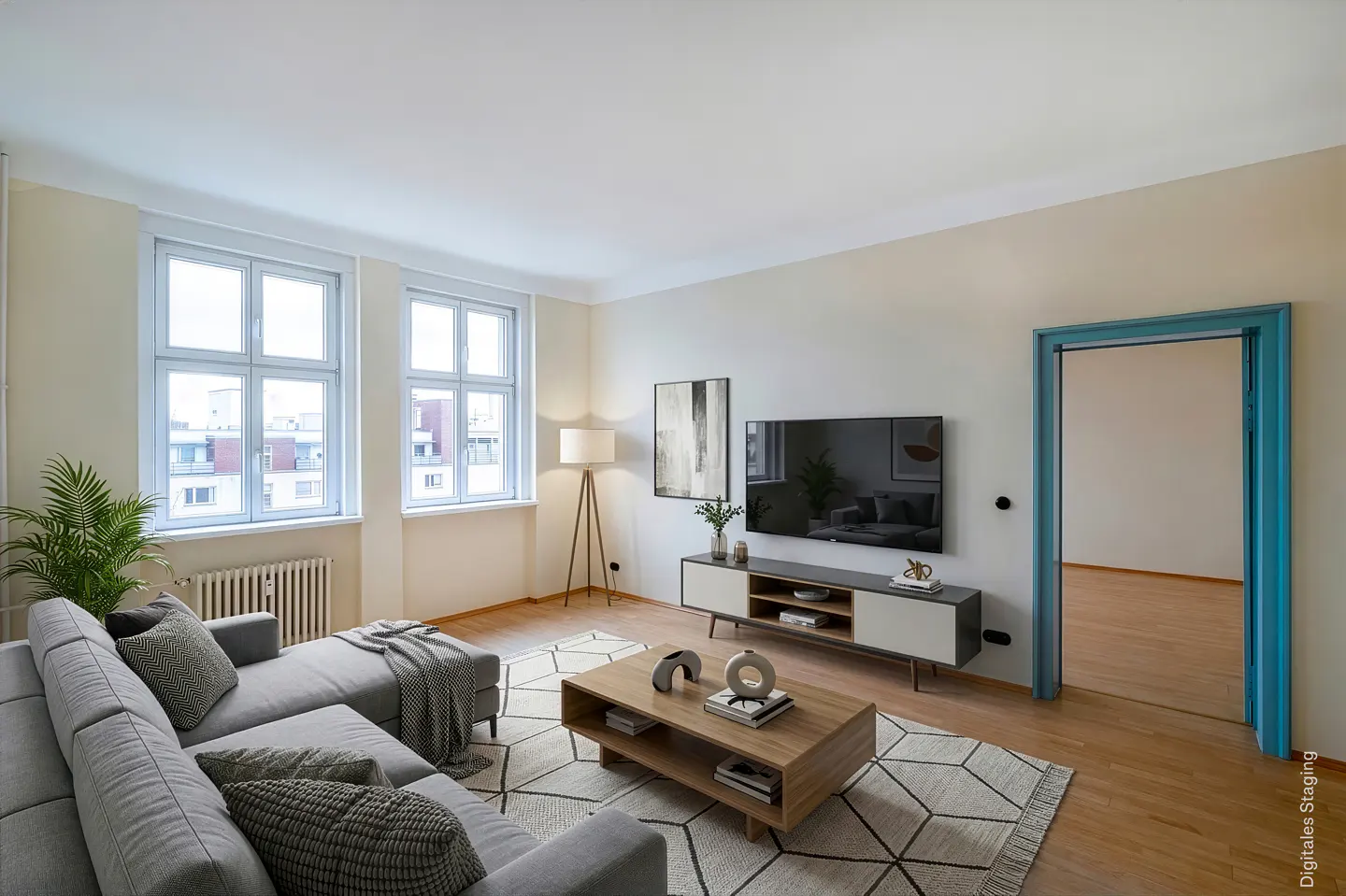 Bright living room with a gray sectional sofa, wood coffee table, TV, and a blue door frame. Two large windows let in natural light.