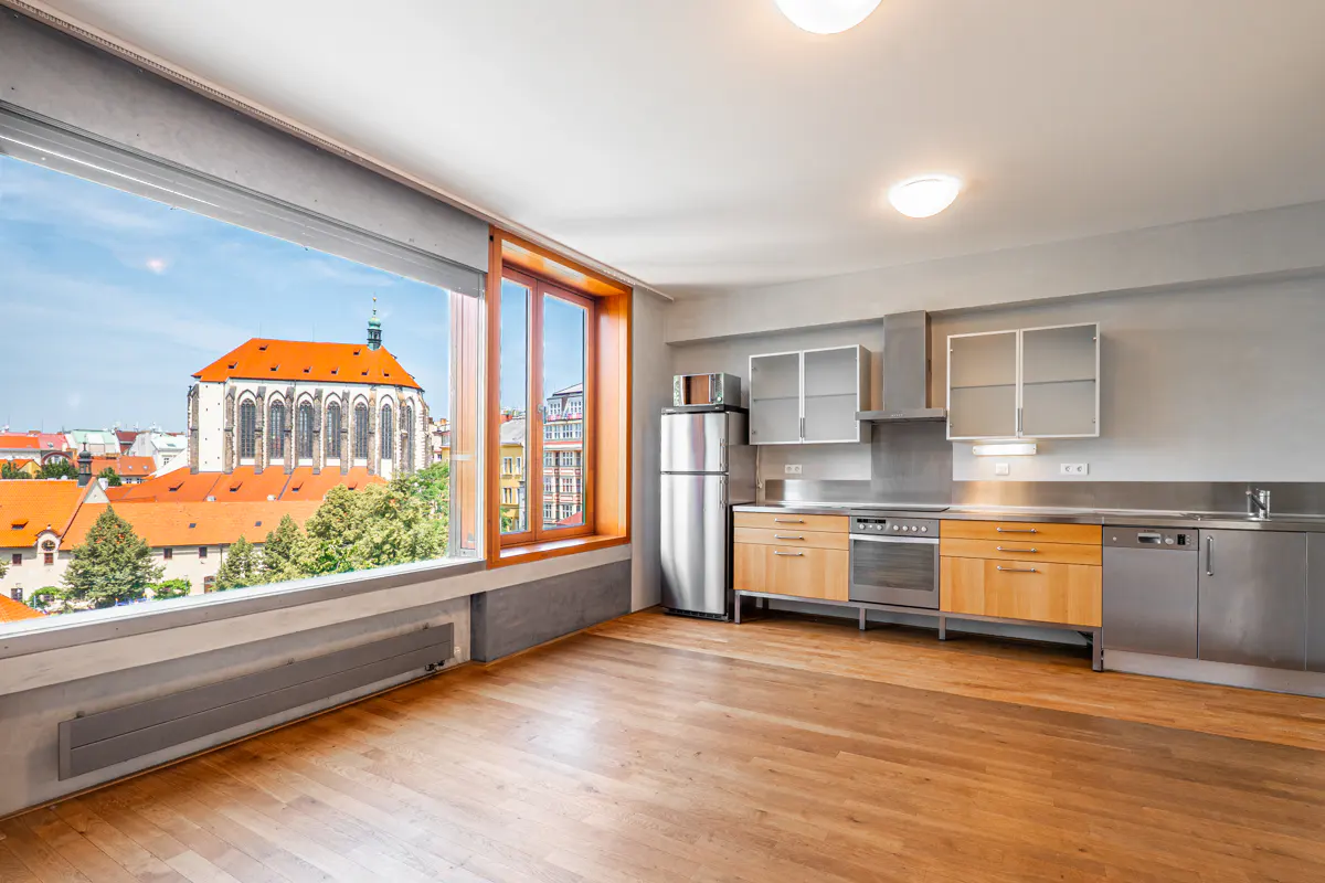 Bright, empty apartment with wood floors, stainless steel appliances, and a large window with a view of a church.