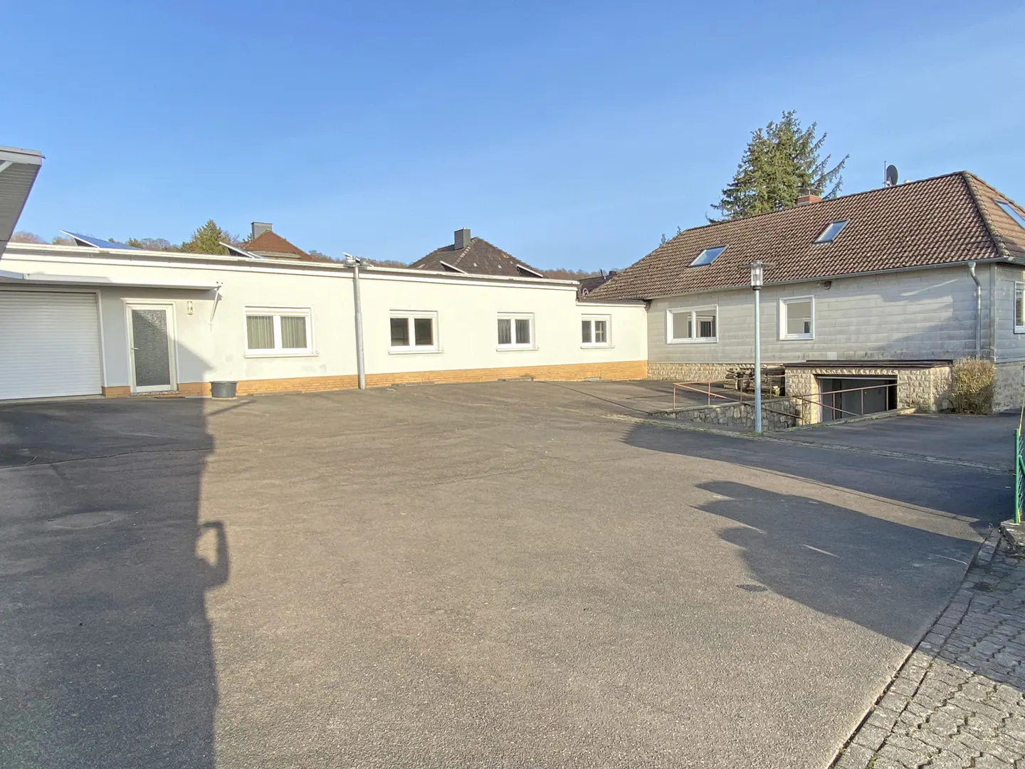 Exterior view of a white building with a large parking lot and a house with a brown roof.