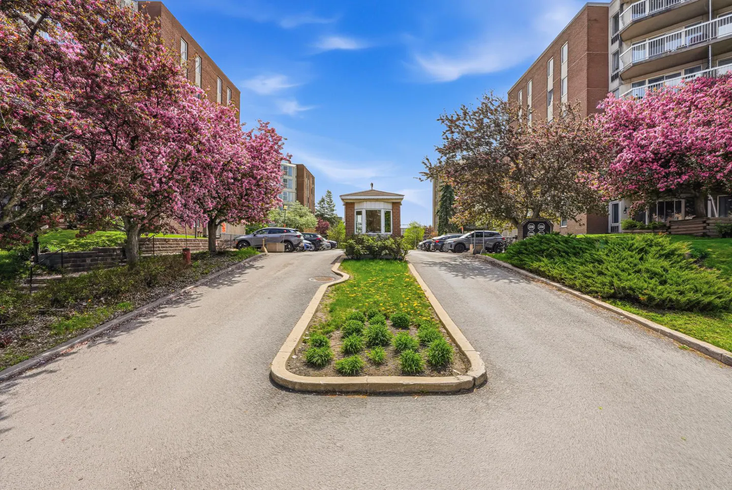 Exterior shot of a brick apartment complex with pink flowering trees and a guardhouse.