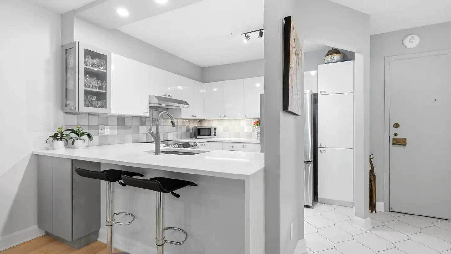 A modern kitchen with white cabinets, a gray accent wall, and two black bar stools at the island.