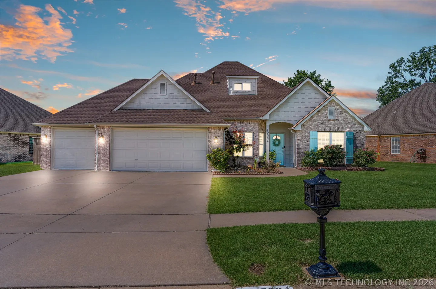 Single-story brick home with a three-car garage, blue front door, and a decorative mailbox at sunset.