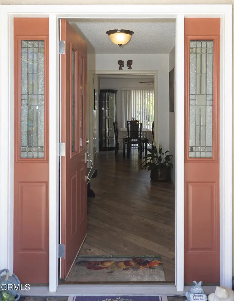 Open salmon-colored front door with glass panels, white trim, and a view into a dining room with wood floors.