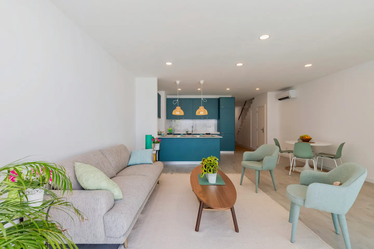Bright, open-concept living space with a gray sofa, teal kitchen island, and light green chairs. A wooden coffee table sits on a white rug.