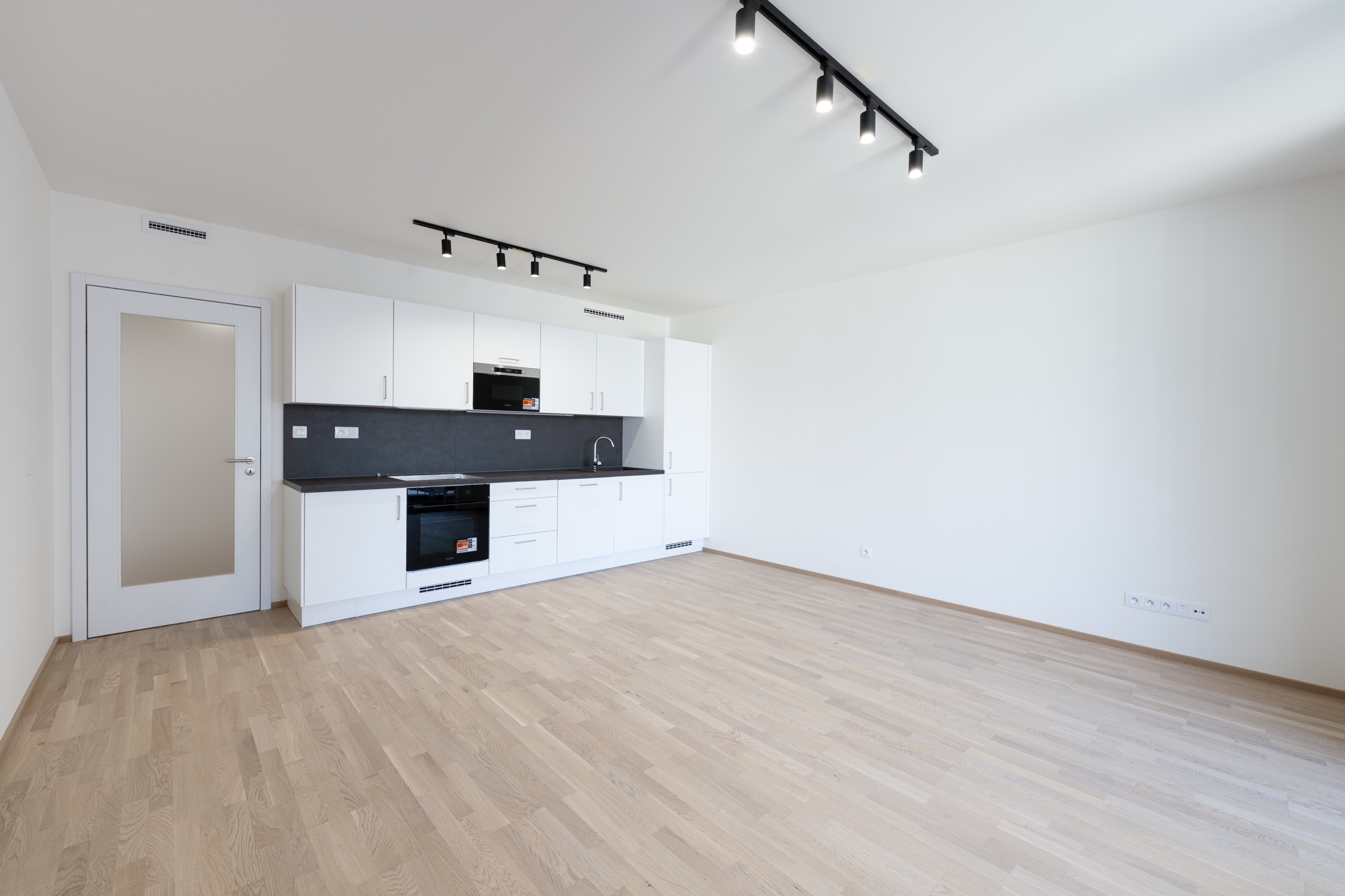 Modern kitchen with white cabinets, dark countertops, built-in appliances, and track lighting over light wood floors. [AI-generated text]