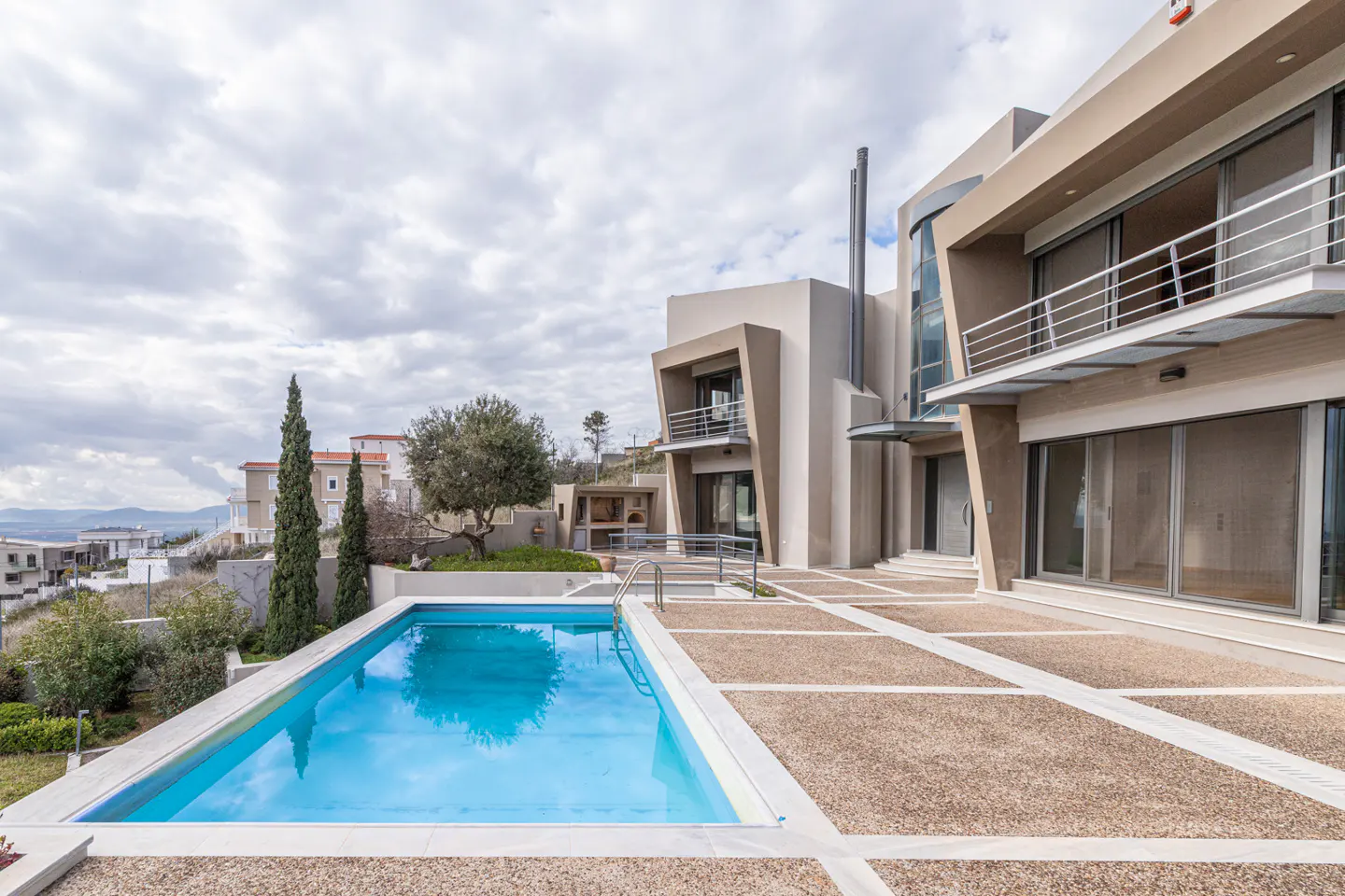 Modern beige house with a blue pool and a stone patio under a cloudy sky.