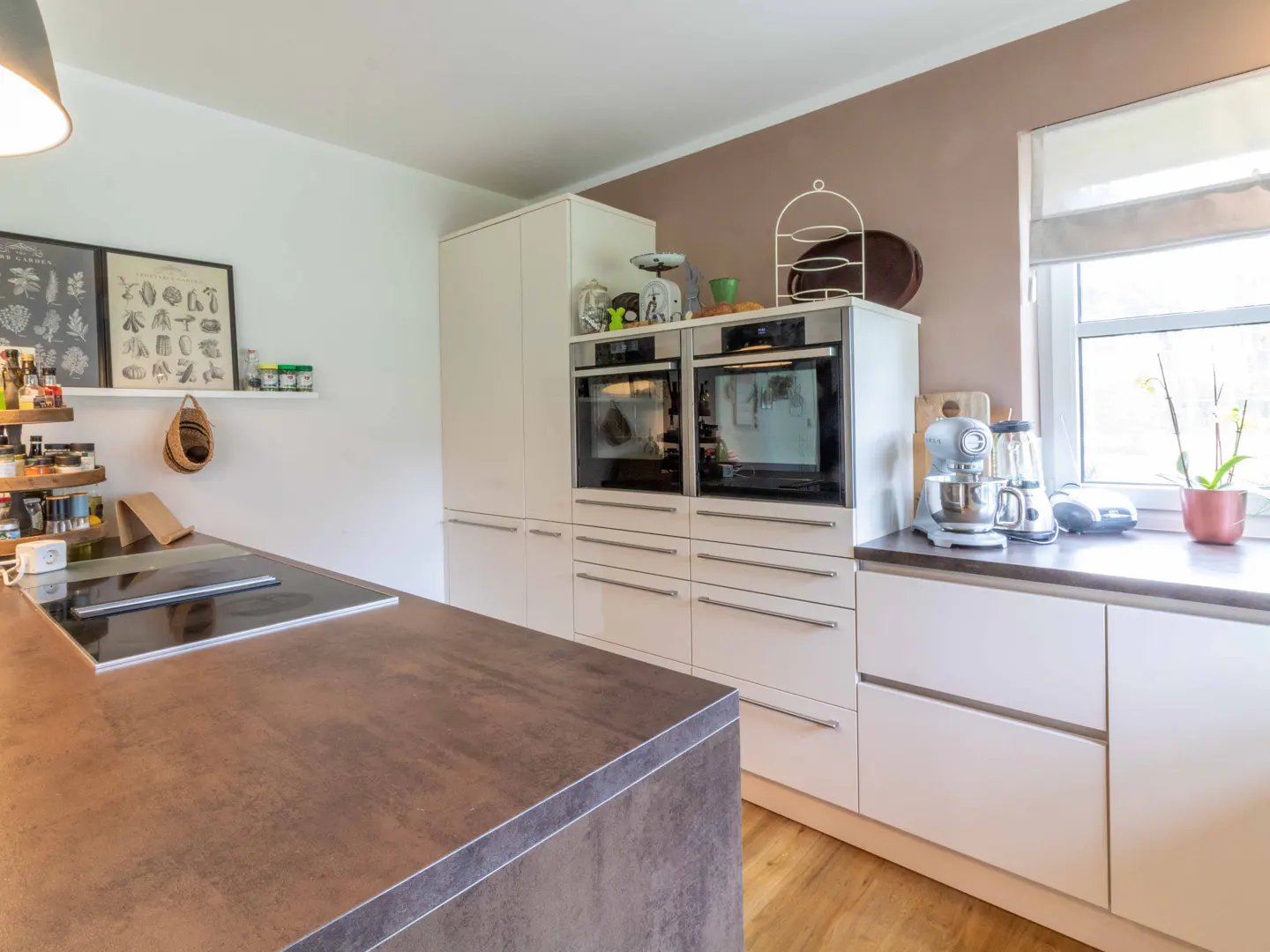 Modern kitchen with a brown island, white cabinets, and stainless steel appliances. Natural light streams through a window.