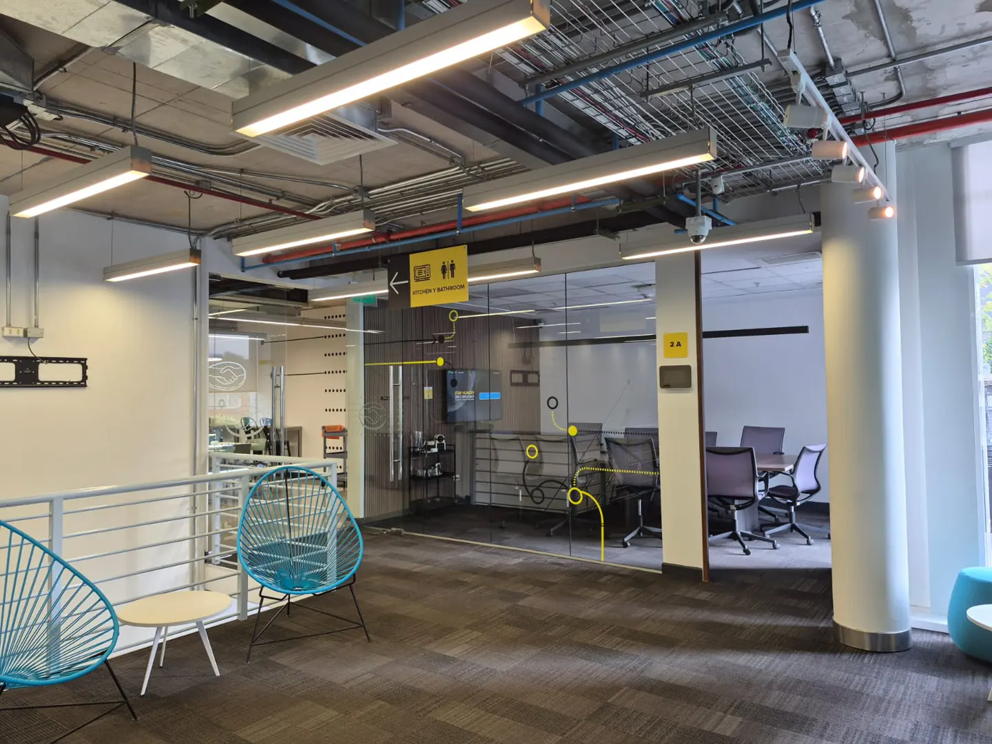 Office space with blue chairs, a small table, and a glass-walled conference room with a table and chairs.