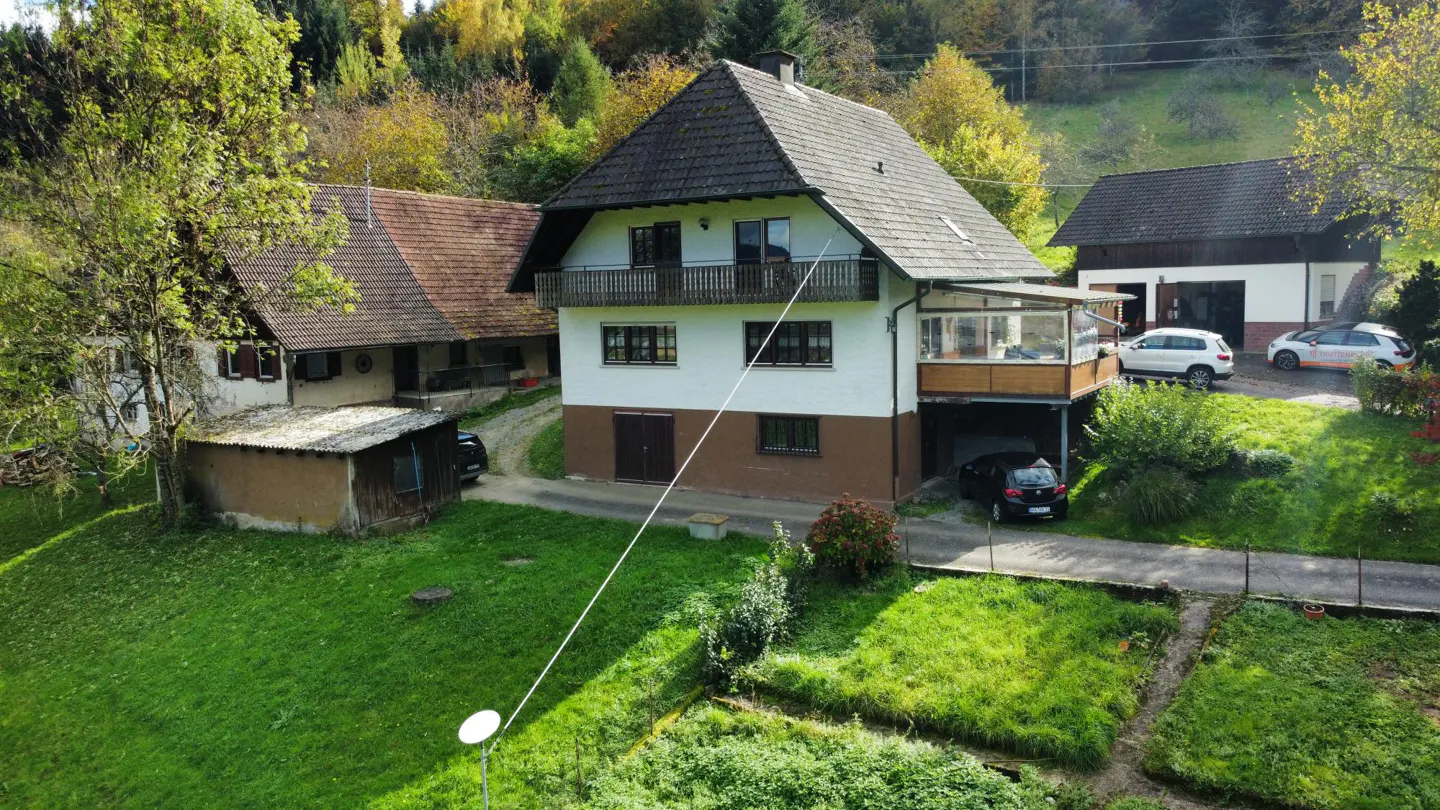 A two-story white house with a brown roof and balcony, surrounded by green grass and trees.