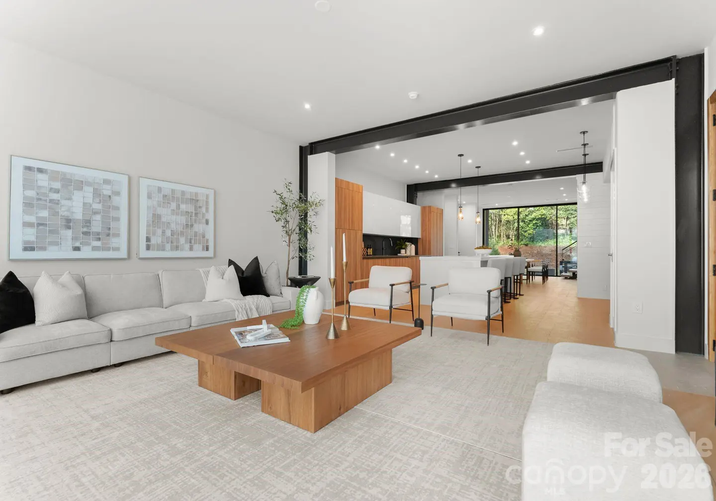 Modern open-concept living room with a light gray sofa, wooden coffee table, and view into a sleek kitchen.