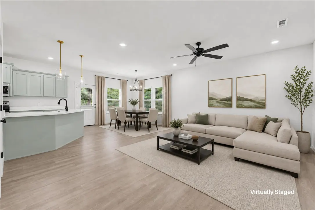 Open-concept living space with a kitchen island, dining table, and a beige sectional sofa. Two landscape paintings on the wall.