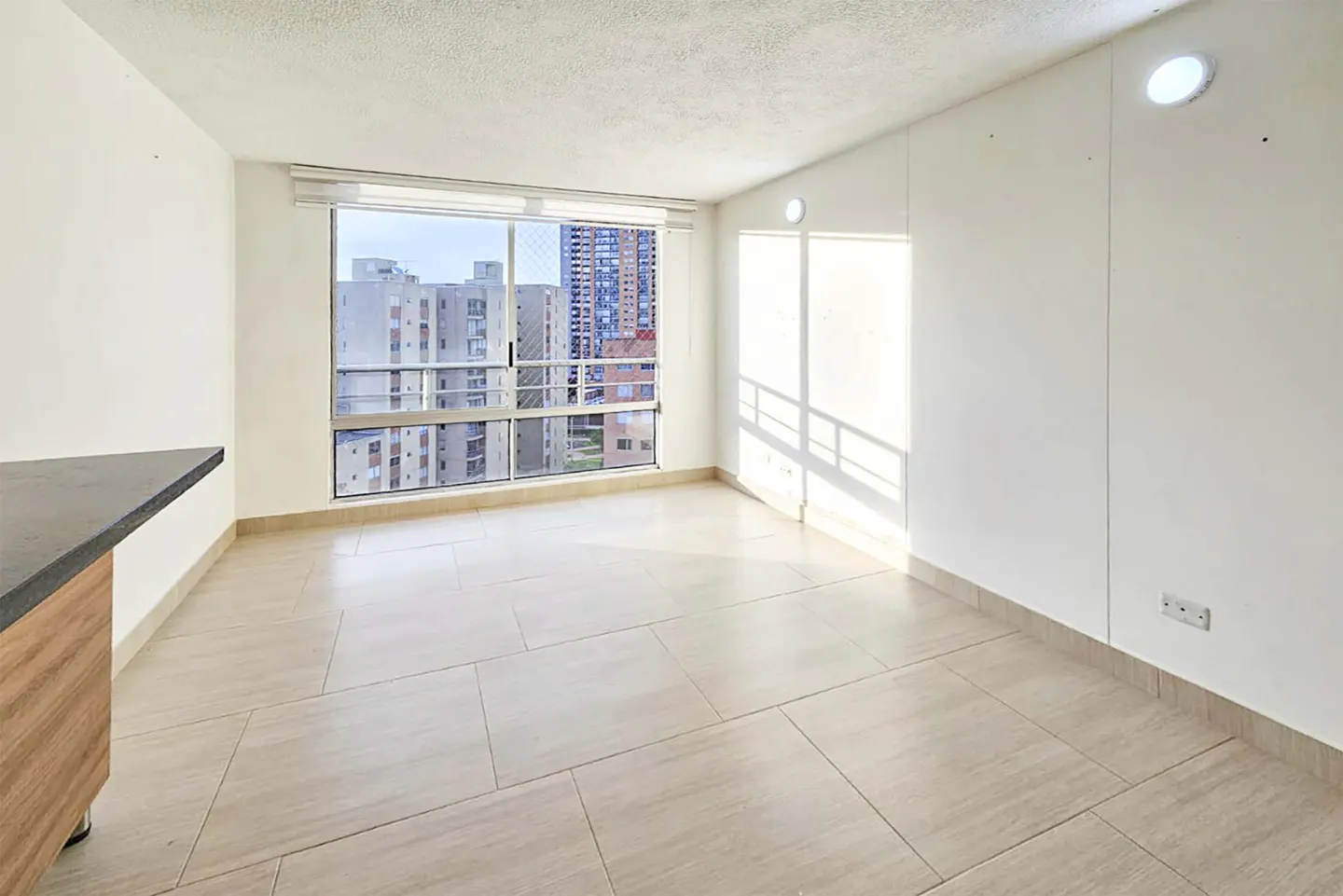 Bright, empty room with beige tile floor, white walls, and a large window showing city buildings.