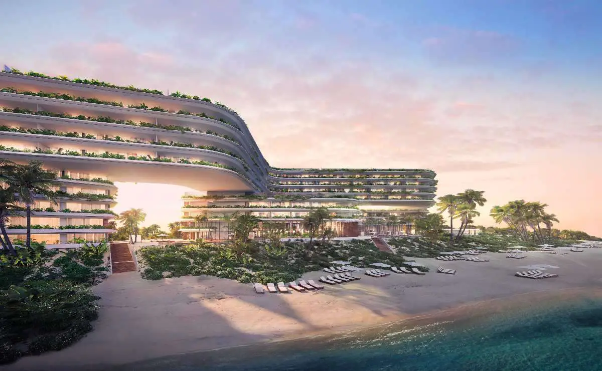Modern beachfront hotel with curved architecture and greenery on balconies, facing a sandy beach with lounge chairs.