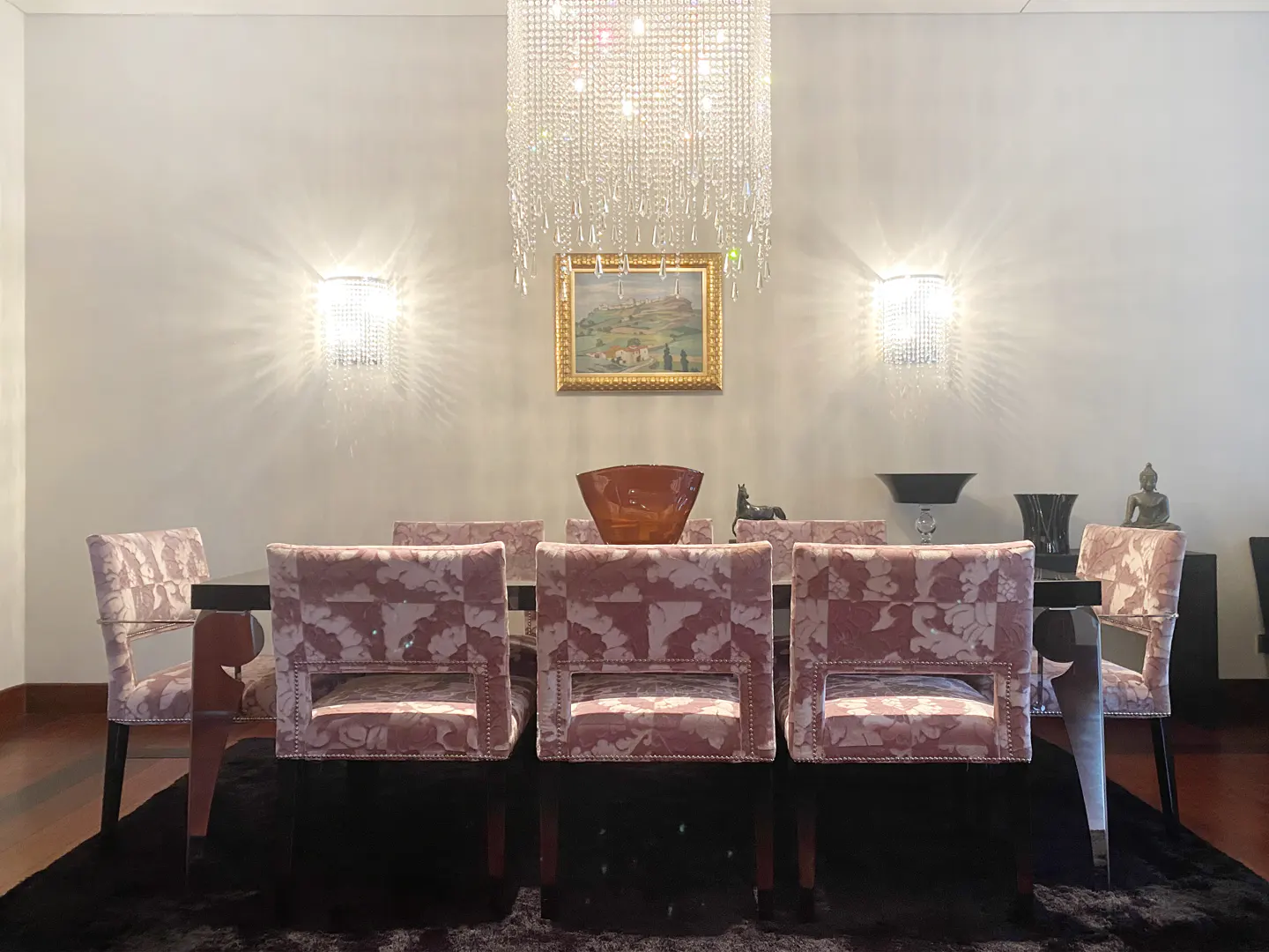 Formal dining room with a black table, floral upholstered chairs, crystal chandelier, and wall sconces.