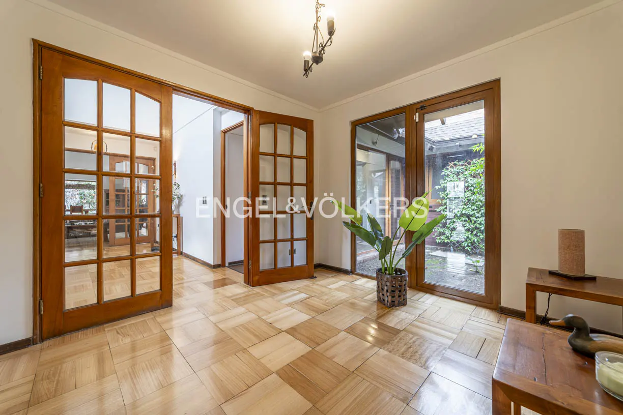 A bright foyer with wood-framed glass doors, a parquet floor, and a potted plant. Natural light streams in from the courtyard view.