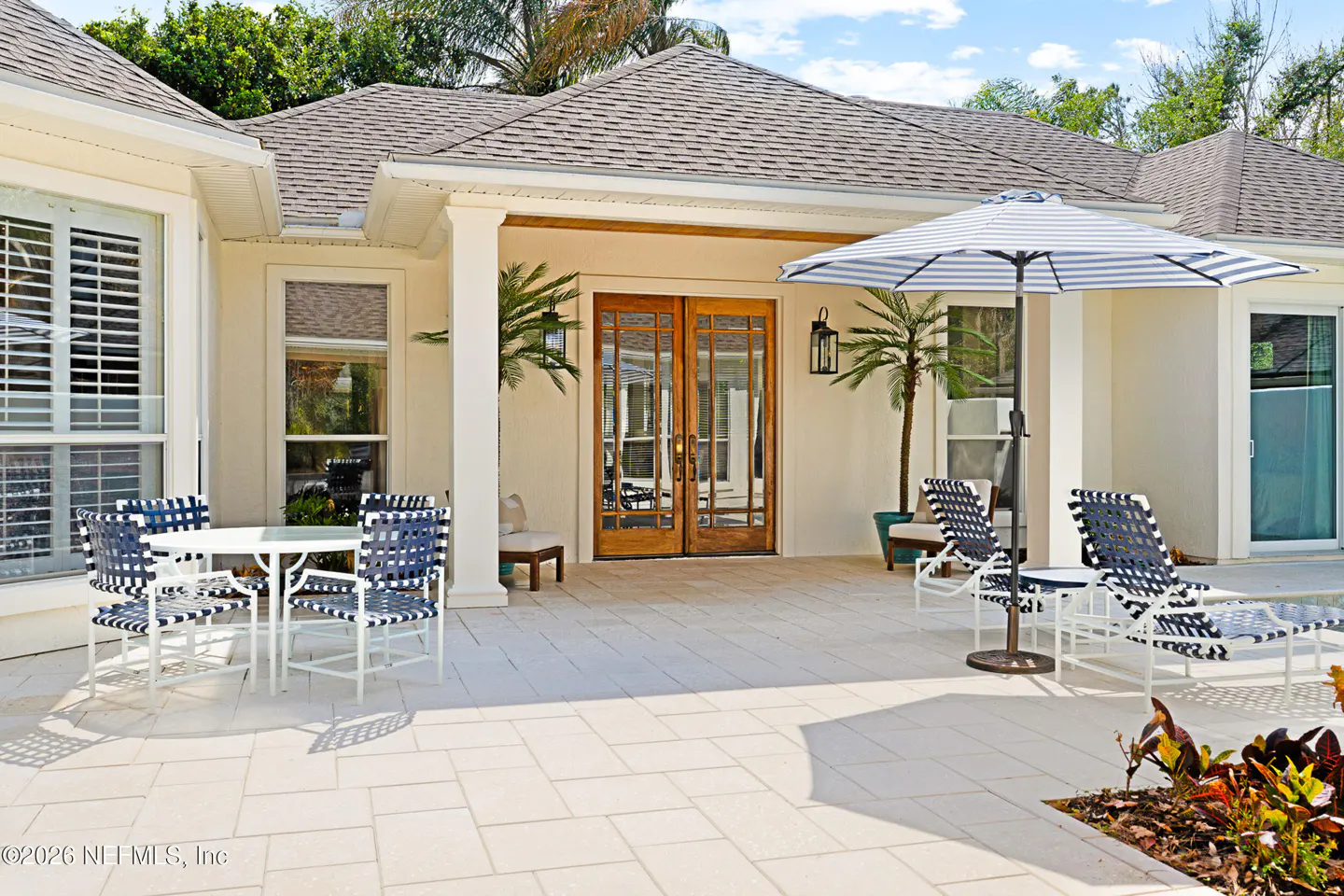Outdoor patio with table, chairs, lounge chairs, and umbrella. Double doors lead into the house.