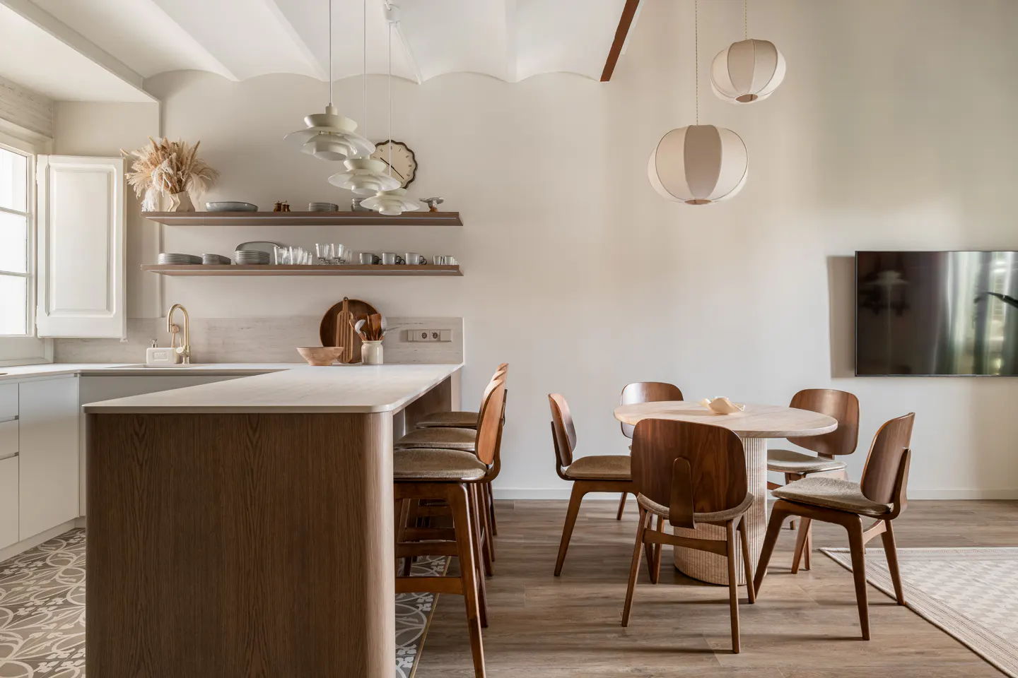 A bright, modern kitchen with a white countertop island, wooden bar stools, and a round dining table with four chairs.