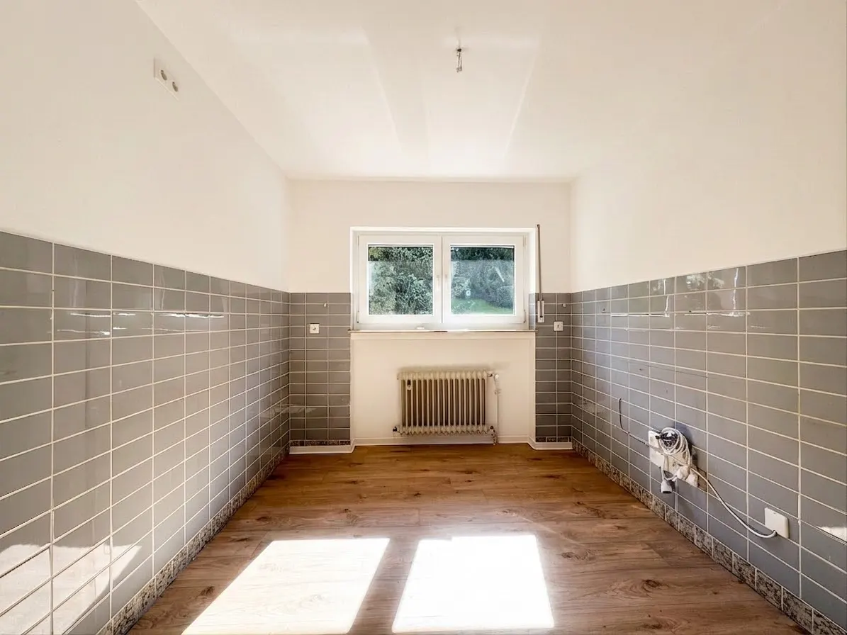 Empty room with wood floor, gray tiled walls, and white upper walls. A window is centered with a radiator below.