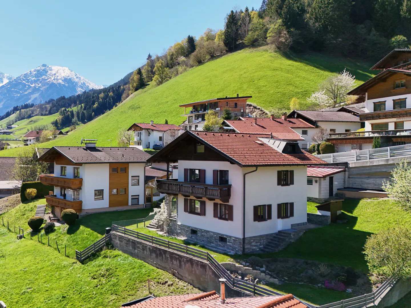 Scenic view of white houses with red roofs nestled on a green hillside, with snow-capped mountains in the background.