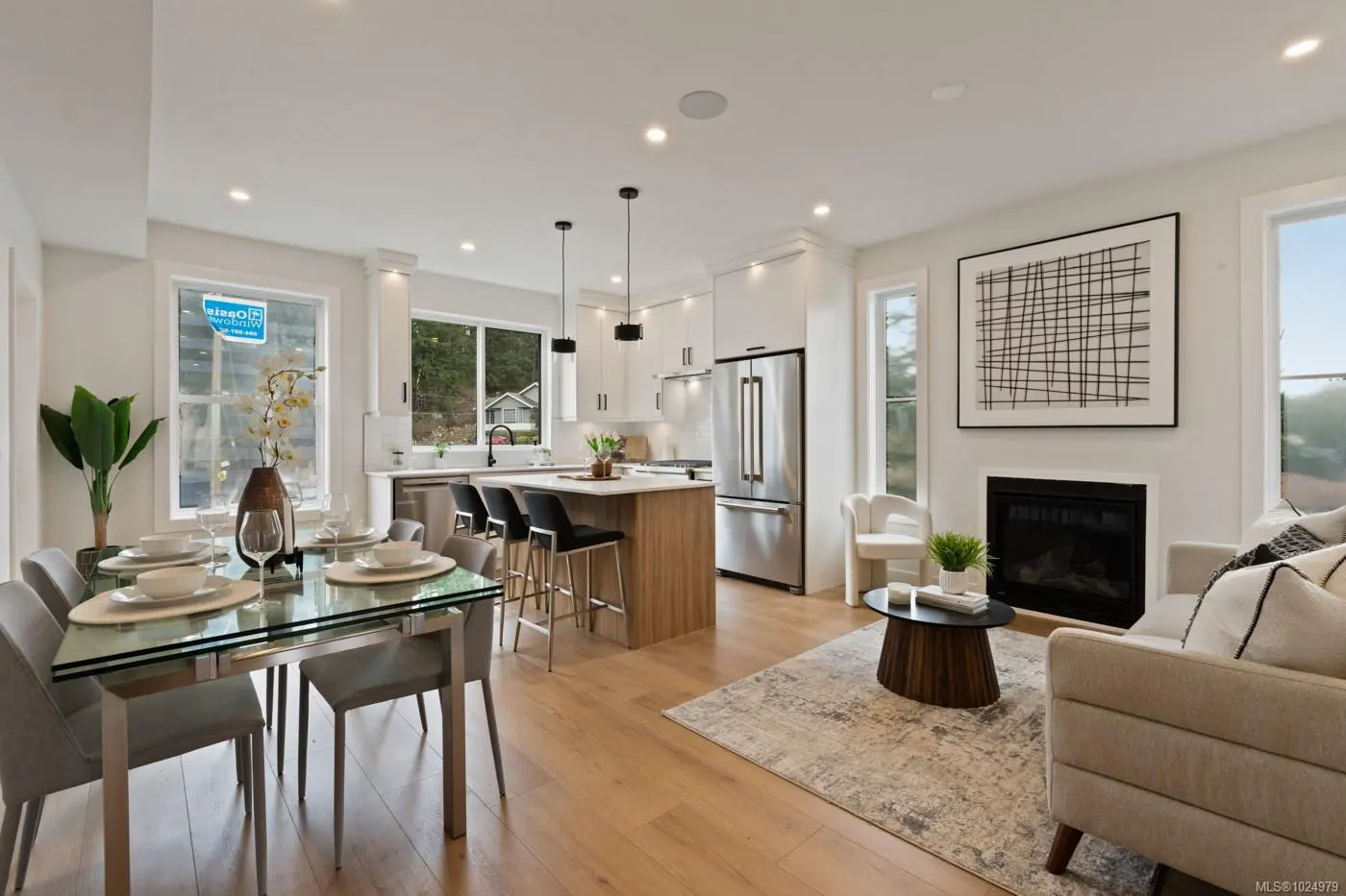 Bright, open-concept living space with a glass dining table, kitchen island with black stools, and a cozy living room with a fireplace.